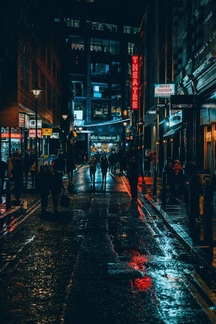 Hình ảnh chill đường phố đêm mưa với ánh đèn neon và người đi bộ trên vỉa hè.