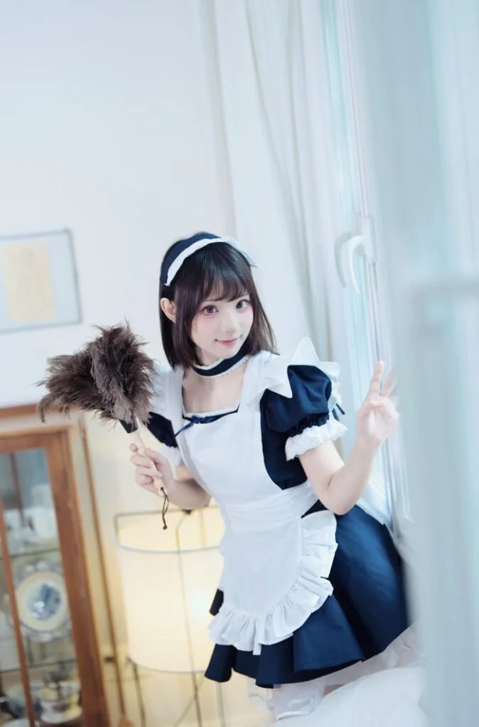 Cô gái trẻ xinh xắn trong bộ cosplay hầu gái cầm chổi lông gà