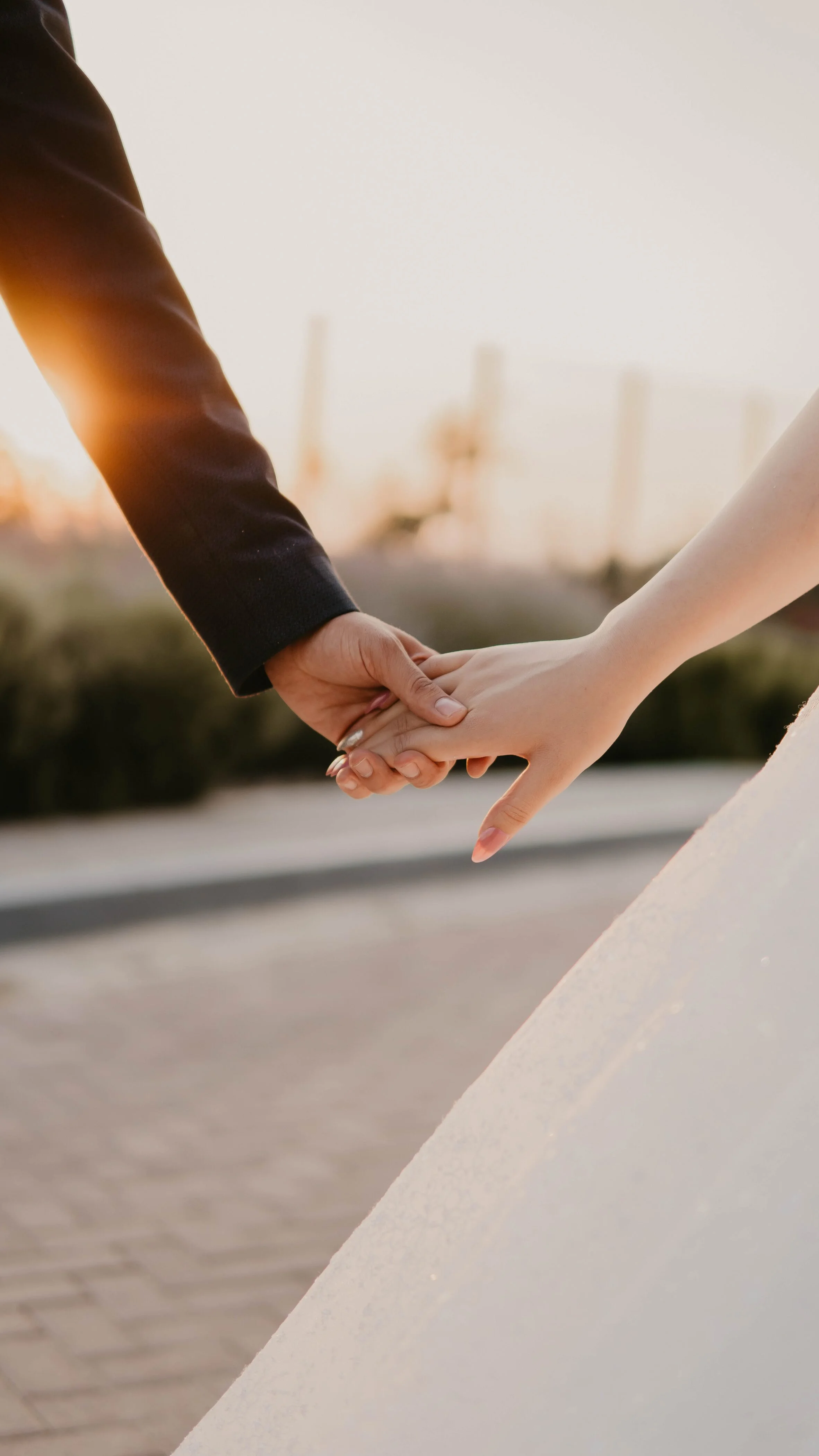 Cặp đôi nắm tay nhau trong trang phục cưới dưới ánh nắng chiều.