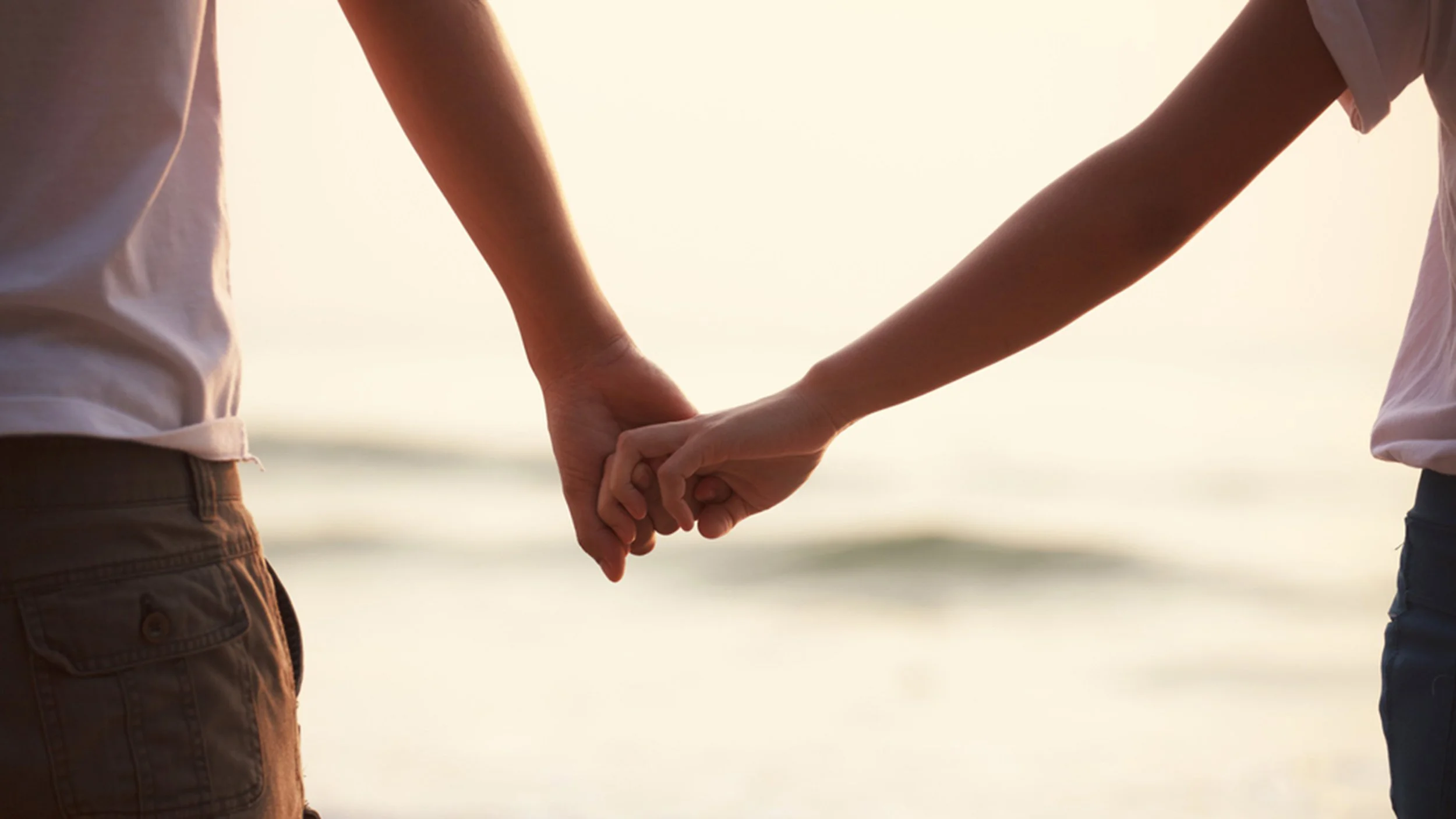 Đôi tình nhân nắm tay nhau đi dạo trên bãi biển lúc hoàng hôn.